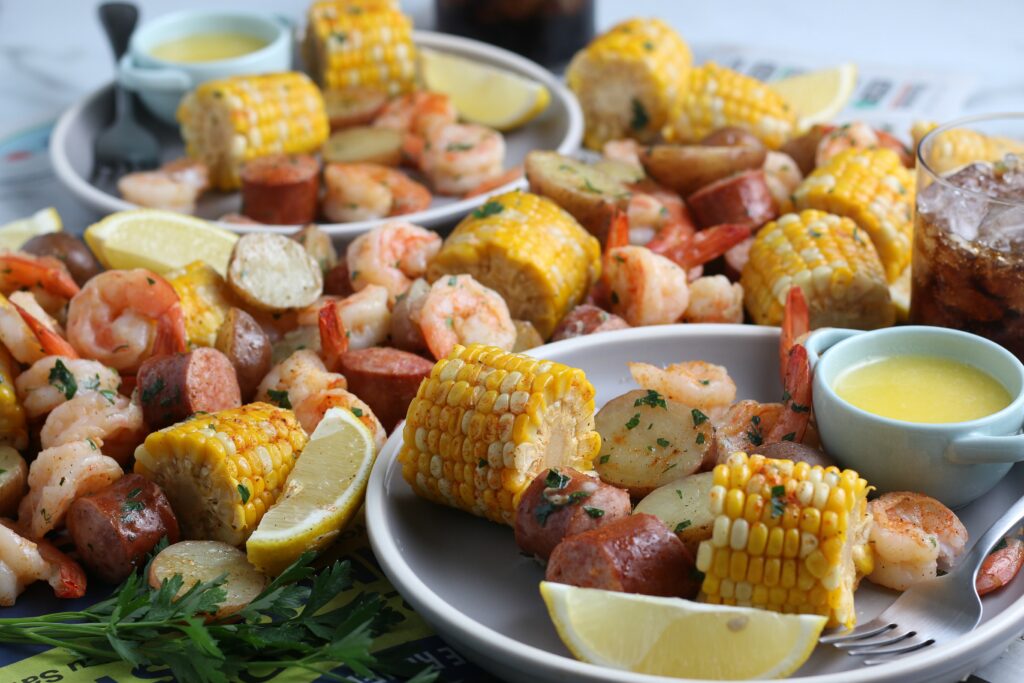 Shrimp boil made with corn, potatoes and sausage, and served with butter and lemons on a white plate