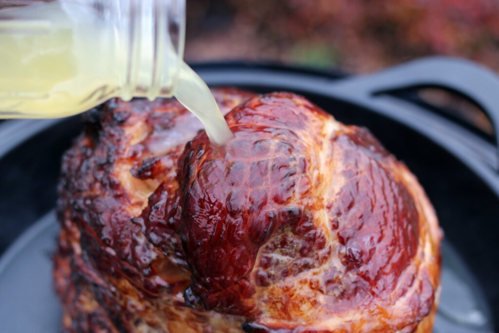 pouring chicken stock over the smoked ham