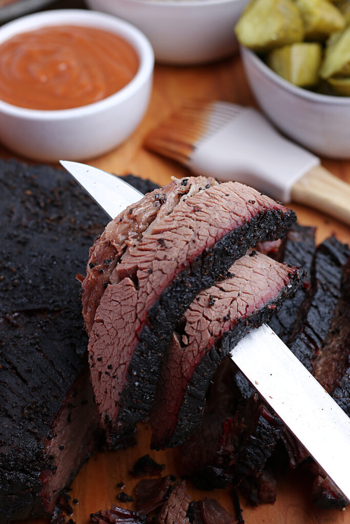 smoked brisket being served over knife with pickles and barbecue sauce