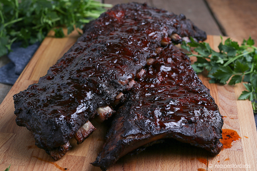 Cooked Baby Back Ribs served with parsley on a wooden cutting board