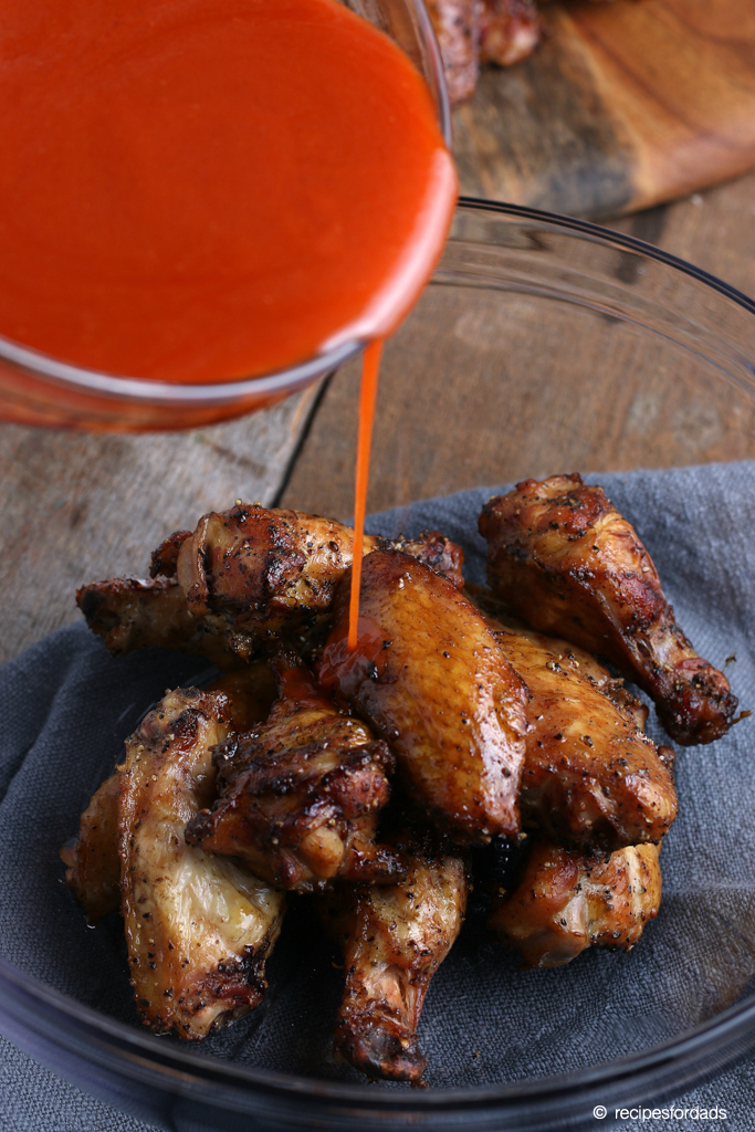 pouring buffalo sauce over smoked chicken wings 