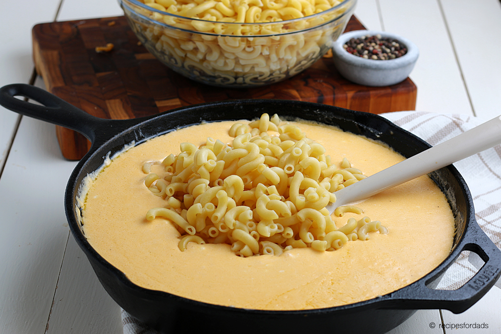 mixing noodles with cheese in cast iron skillet