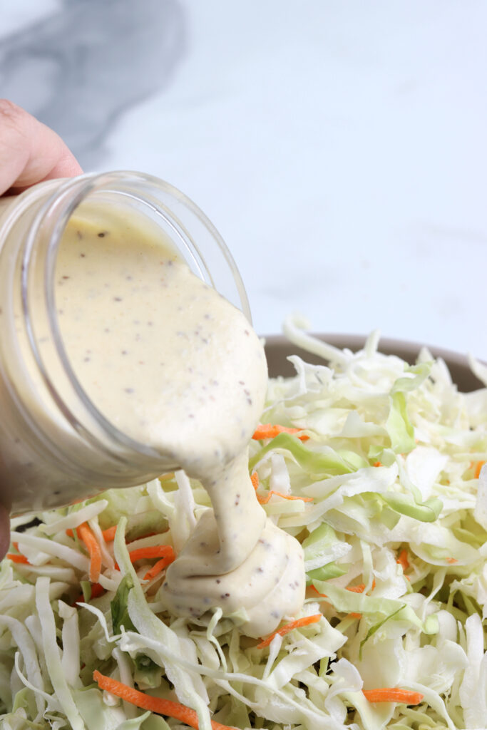 pouring homemade coleslaw dressing over cabbage