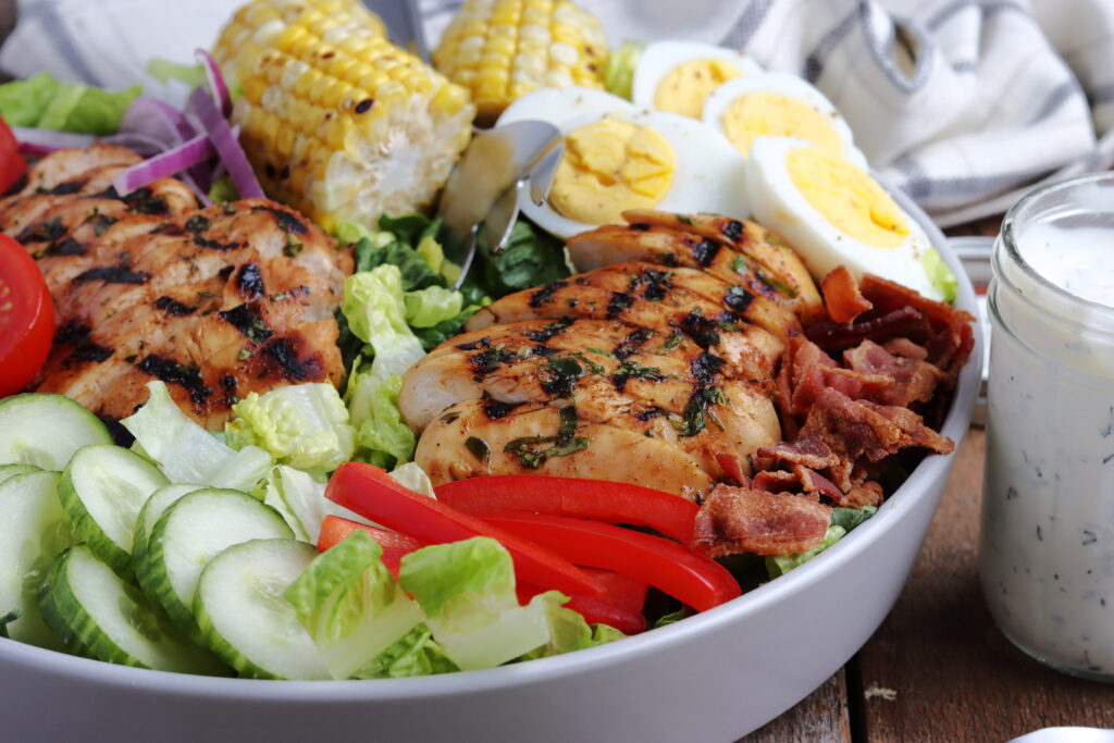 delicious grilled chicken cobb salad served with corn on the cob and boiled eggs.