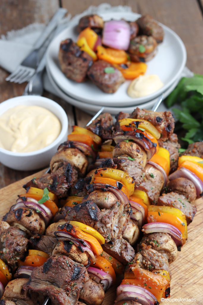 beef kabobs served on skewers, cutting board with white plate and sauce