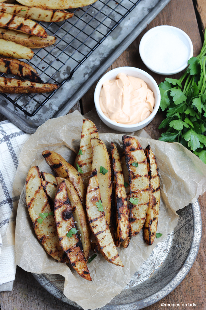 grilled potato wedges served on brown cutting board with dipping sauce