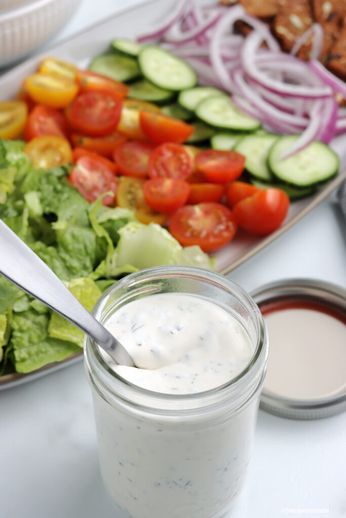 homemade ranch dressing in a small glass jar, served with lettuce and fresh veggies