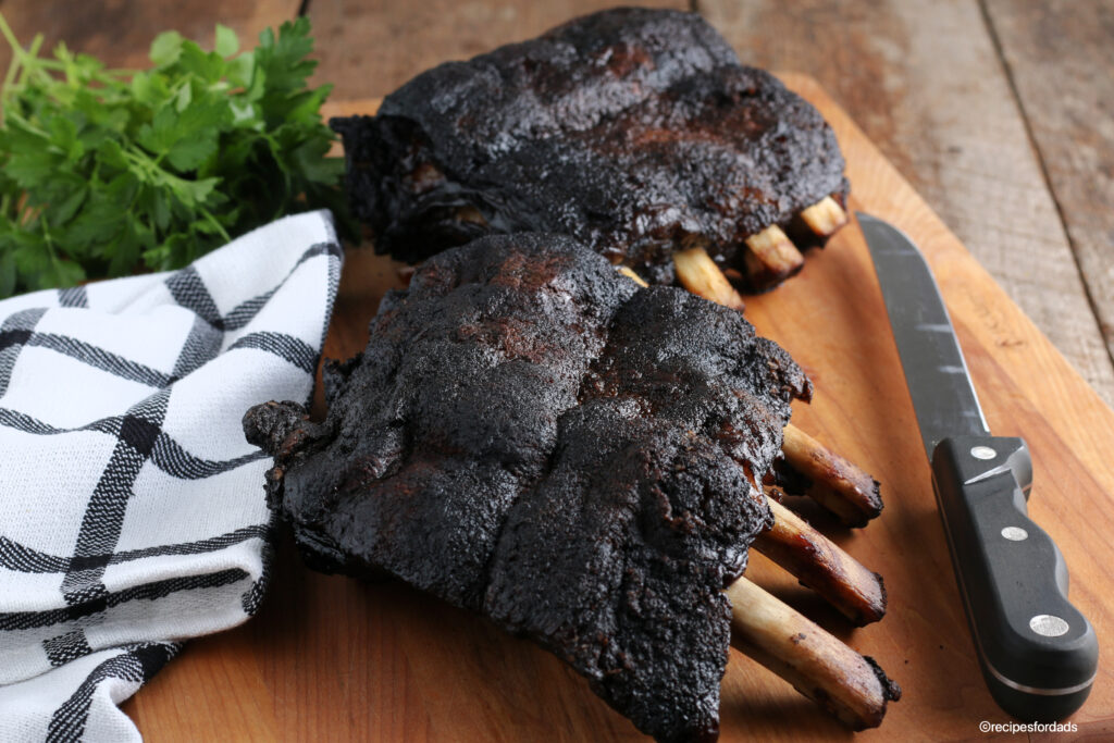 Smoked beef ribs served on cutting board with knife and black & white napkin