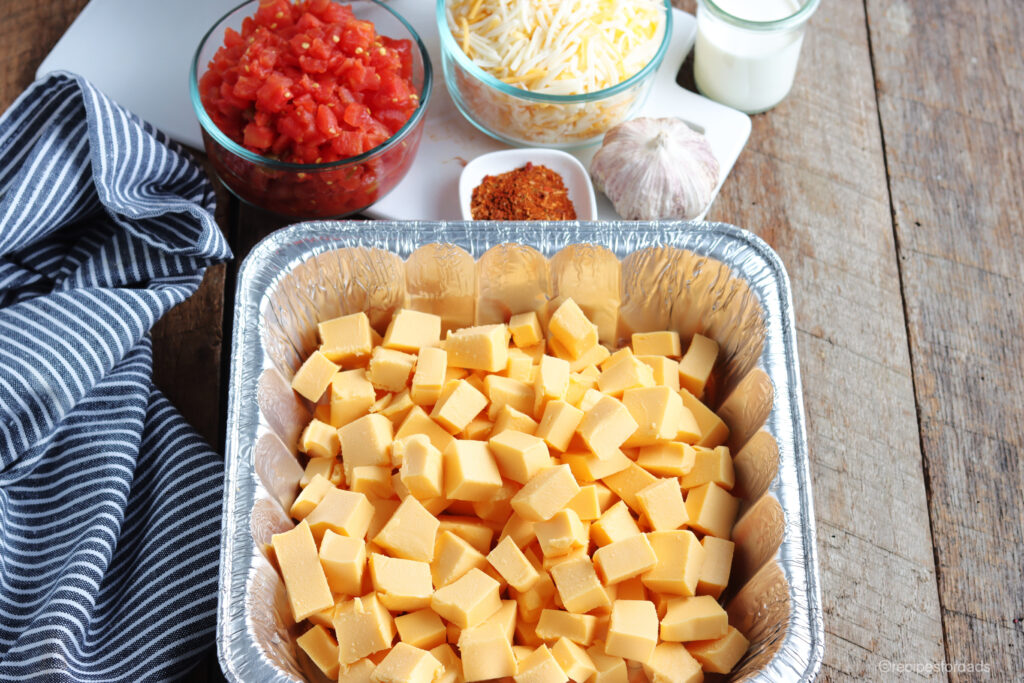 cubed cheese in an aluminum pan, paired with tomatoes and seasoning