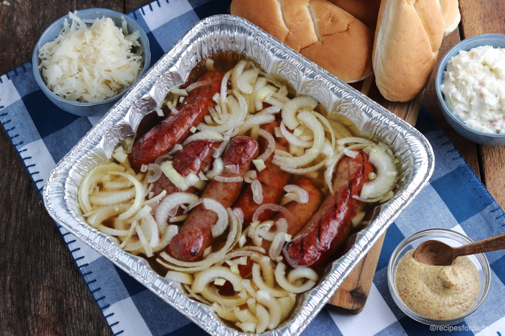 Brats in beer bath in aluminum pan.