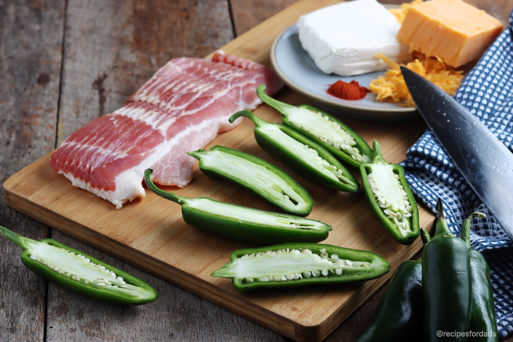 Jalapenos cut in half with bacon slices on a serving board