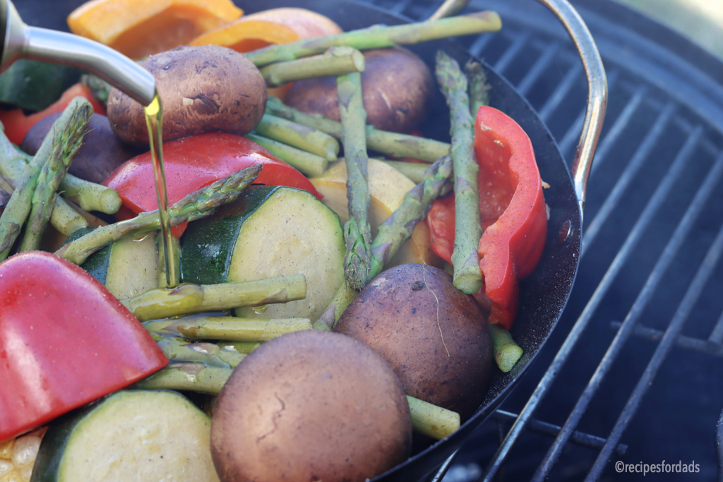 pouring olive oil on mixed vegetables that are on smoker