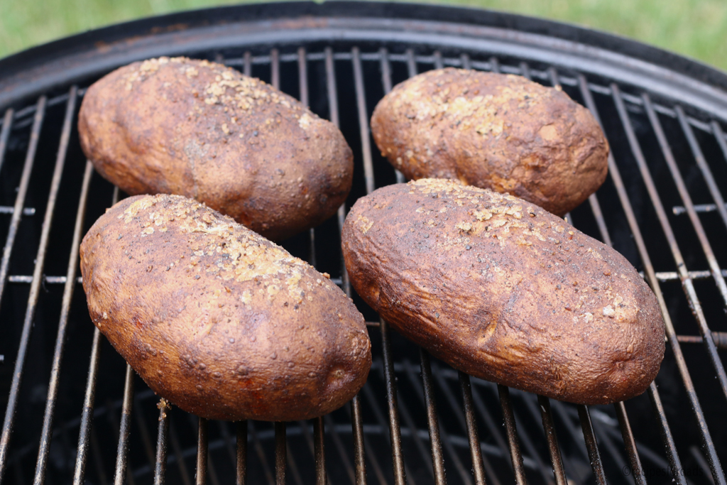 four potatoes smoking over a Weber smoker