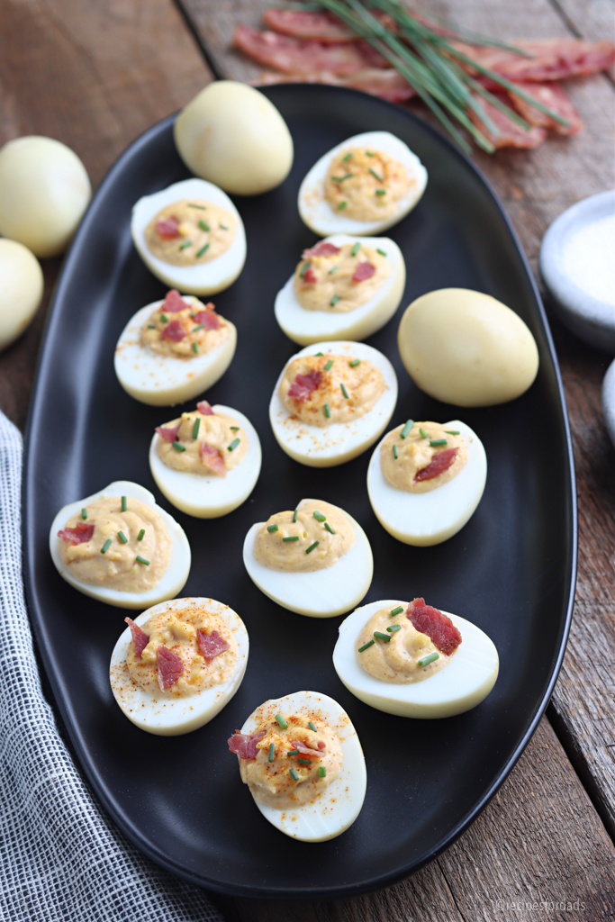 deviled eggs served on black dish garnished with bacon and chives