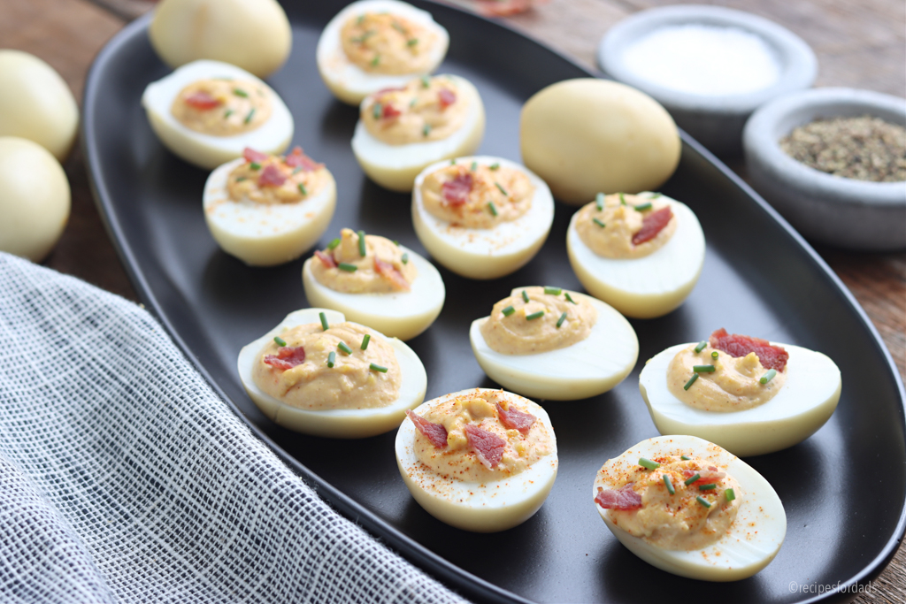 Smoked Deviled Eggs served on black plate with bacon garnish