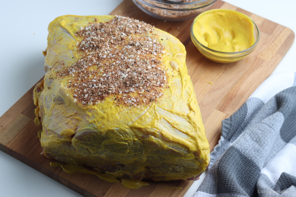 Pork butt covered in mustard and seasoning.