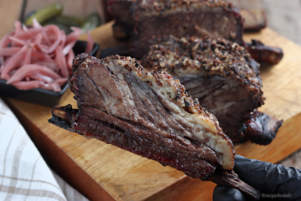 Holding a beef rib and served with pickles and onions