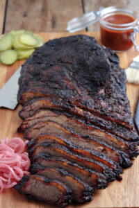 smoked brisket sliced on cutting board with barbecue sauce