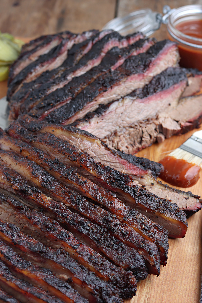 smoked brisket sliced on cutting board with barbecue sauce