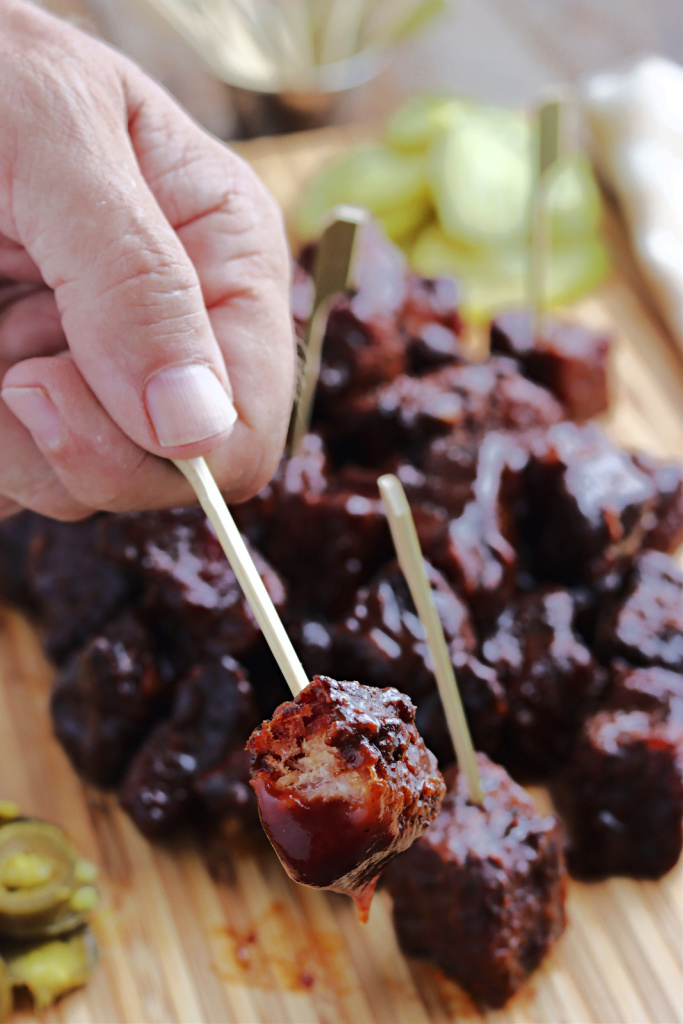 smoked pork belly burnt ends dipped in sauce with toothpicks on cutting board