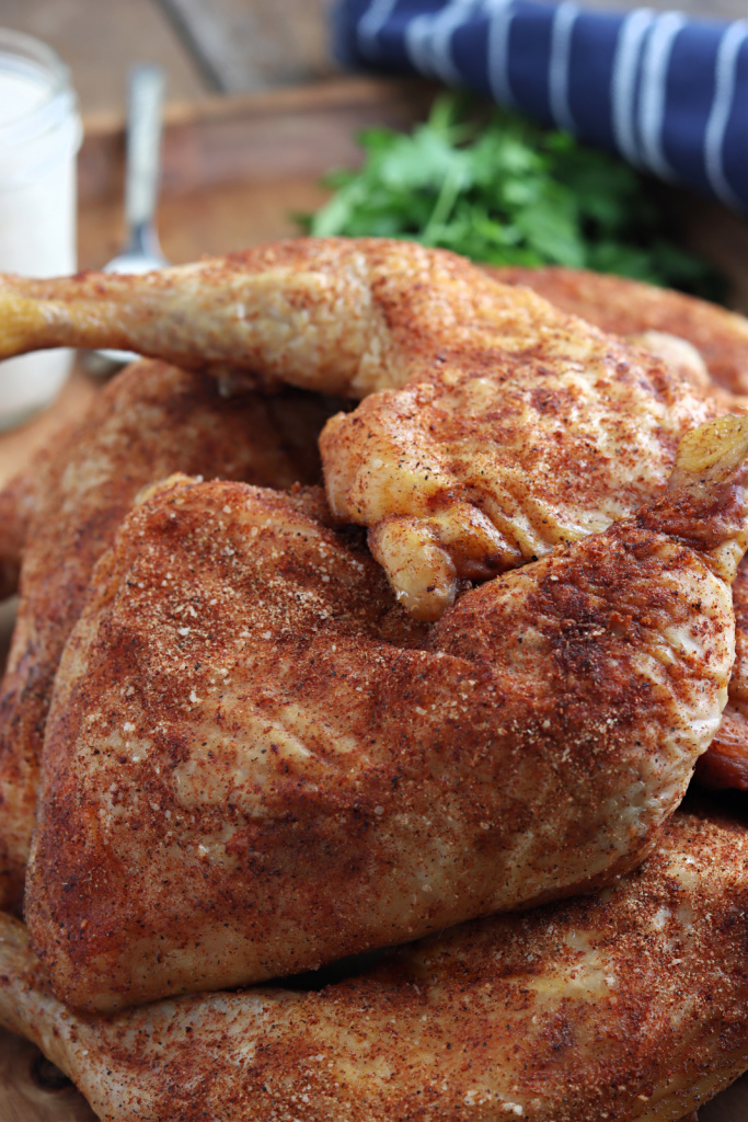 smoked chicken quarters on a wood board with parsley, Alabama white sauce and blue napkin