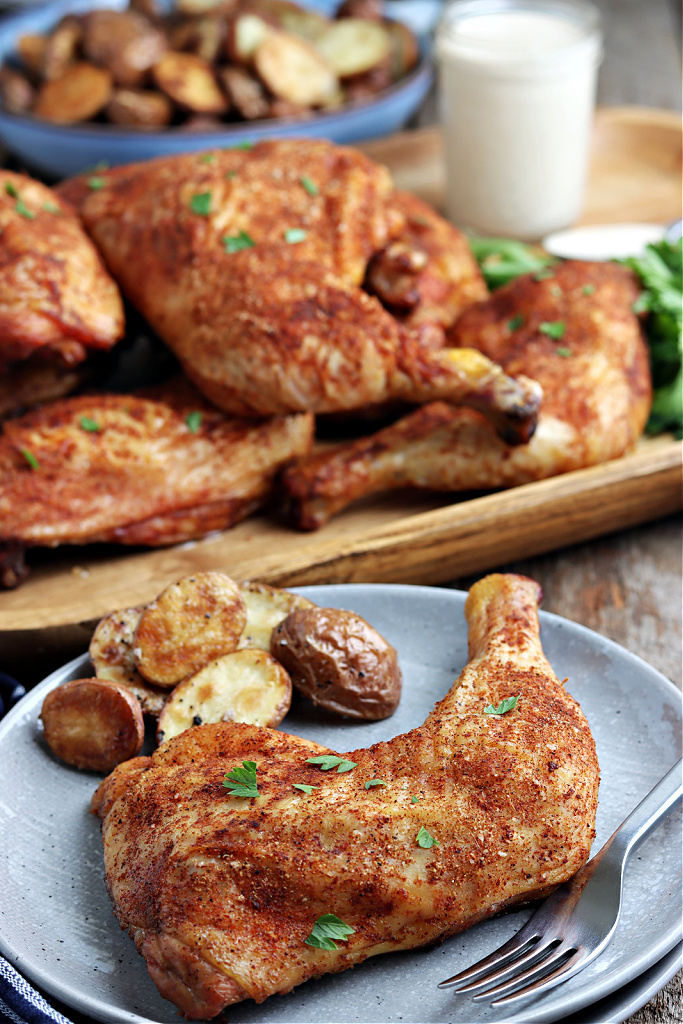 smoked chicken quarters on a wood board with parsley, Alabama white sauce and potatoes on gray plate