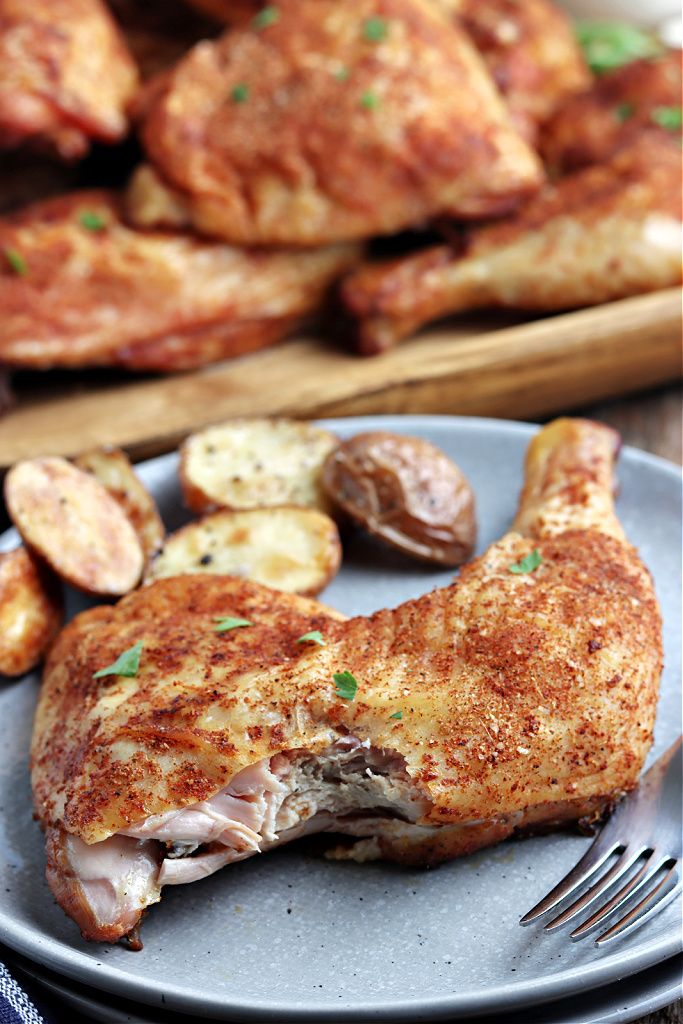 smoked chicken quarters on a wood board with parsley, served on gray plate with potatoes