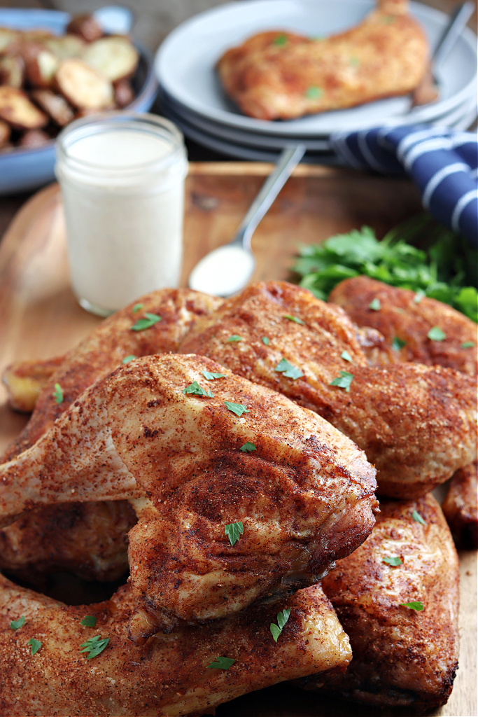 smoked chicken quarters on a wood board with parsley, Alabama white sauce and blue napkin