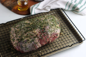 boneless leg of lamb with herbs, salt and pepper on a wire rack