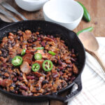 smoked baked beans in cast iron skillet with wooden spoon for serving