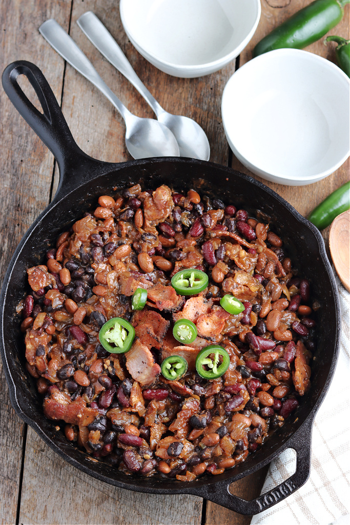 smoked baked beans in cast iron skillet with bowls and spoons