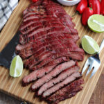 smoked flank steak sliced on cutting board with knife and serving fork
