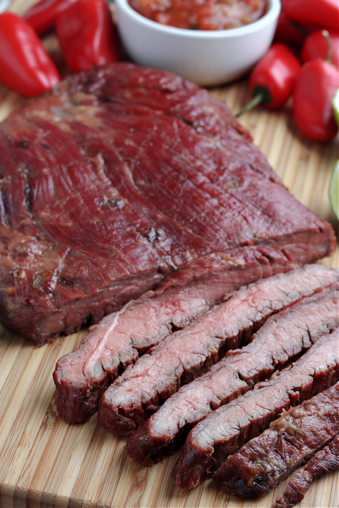 smoked flank steak sliced on board with limes, red peppers and salsa
