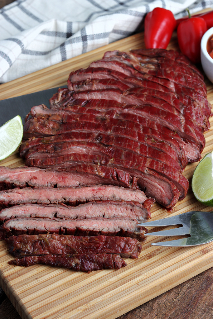 smoked flank steak sliced on board with serving fork